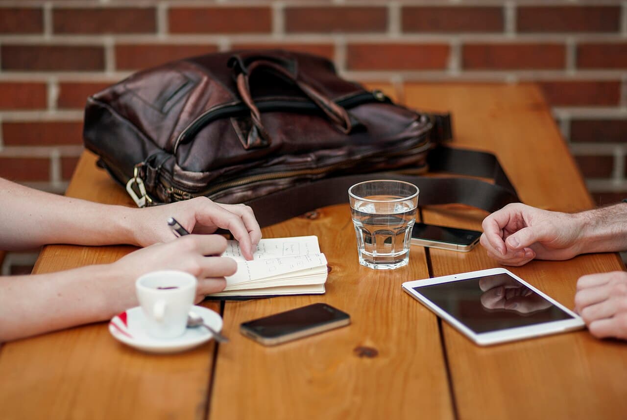 A conversation over coffee, with an open notebook between two people