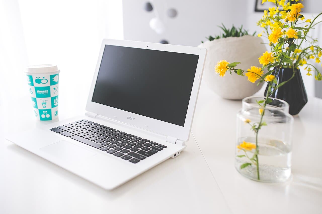 A bright workspace with a laptop, coffee and yellow flowers
